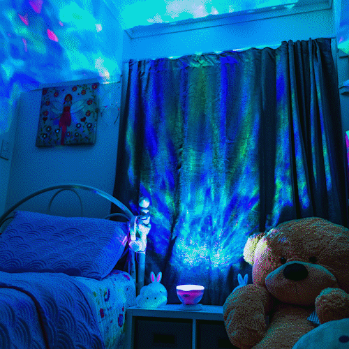 Aurora Skies and Ocean Projector night light showing its range of colours such as blue, purple, green an waving animation projected around a kids room. The room is completely lit up.