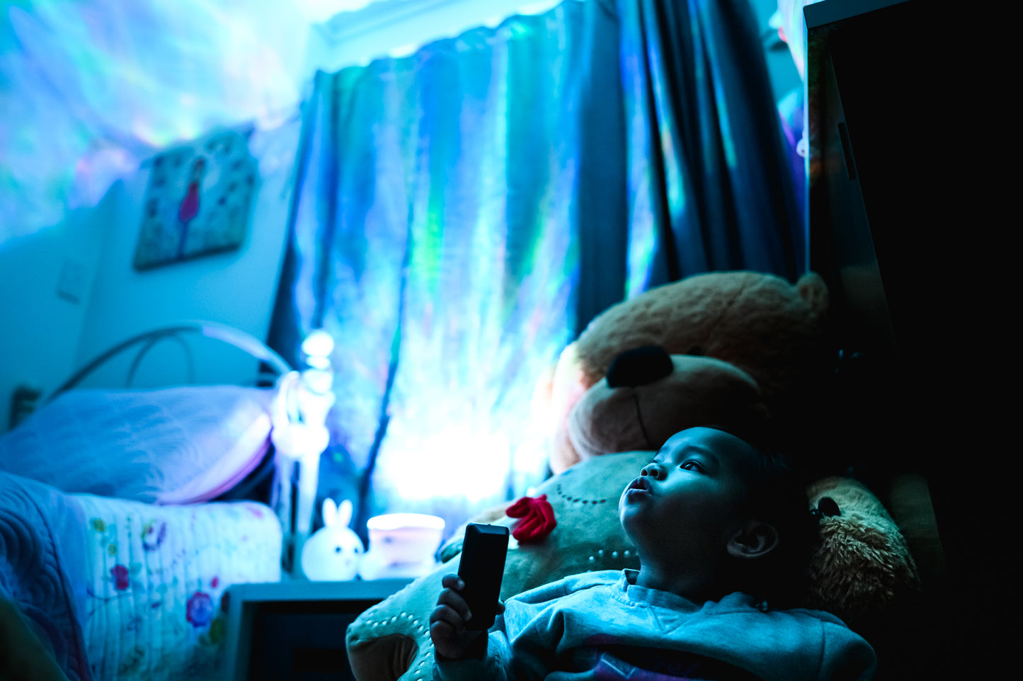 baby with bear toy and aurora skies and ocean night light nz. The kids room is completely lit up with the blue and purple colours