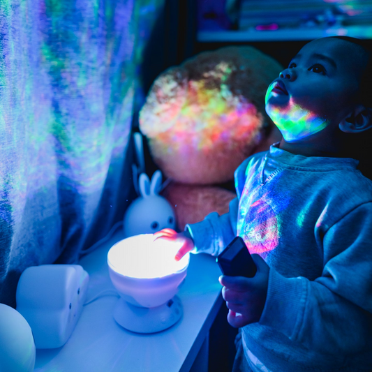 A toddler/kid interacting with the Aurora Skies and Ocean projector. The toddler is looking up to see the wave of colours projected from the night light.